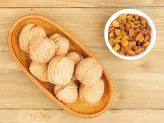 Raisins in a white bowl, walnuts on brown wooden background