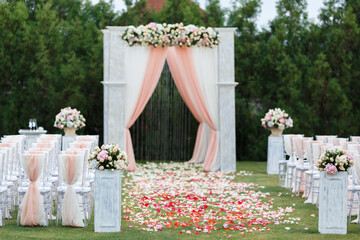 Place for wedding ceremony in white color .White square wedding arch with bouquets of pastel roses in the forest.