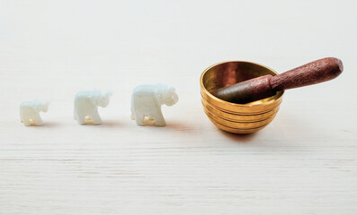 Three elephantes made of stone and singing bowl on white wooden background. Meditation and relaxation concept. Selective focus