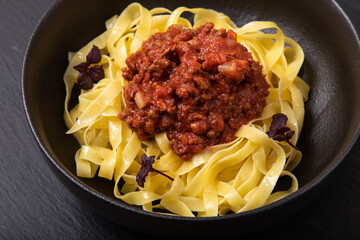Pasta tagliatelle bolognese in a black bowl