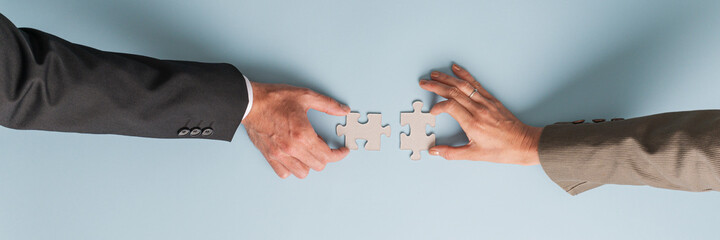 Male and female hand joining two blank matching puzzle pieces