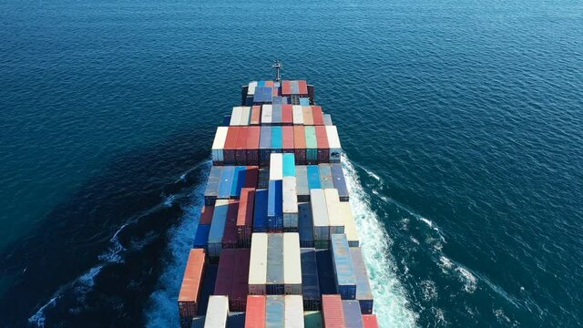 Aerial top down video over Container cargo Ship carrying load in truck-size colourful containers in deep blue open ocean sea 