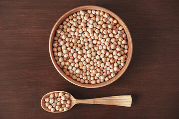 Dry chickpeas in a wooden plate and spoon on a brown wooden background. Top view. Copy, empty space for text