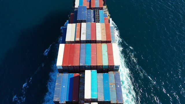Aerial top down video of Container cargo Ship carrying load in truck-size colourful containers in deep blue open ocean sea 