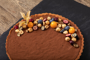 Chocolate tart decorated with fresh berries and cape gooseberry on black slate