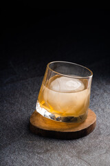 Pouring whiskey from bottle into glass with ice ball on table. Space for text