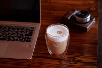 Traveler's breakfast. Cup of cappuccino on wooden table with laptop and photocamera.