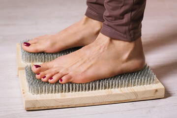 A woman practicing yoga therapy stands on a board with nails. Concept on the topic of massage