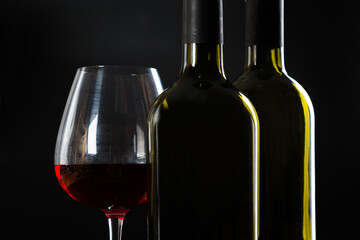 several different bottles of wine and a glass with red wine on a dark glossy background.