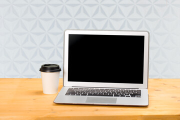 Fototapeta premium Mockup blank laptop screen with coffee on wooden table in coworking space.