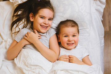 Happy Family Brother and Sister Relaxing Together, Laughing and Playing in Bed in the Early Morning. Healthy Sleep, Wake up, Laugh Concept.