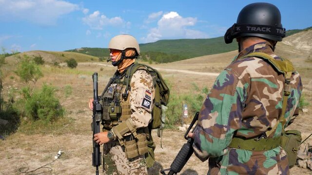 Near military camp staying two soldiers in helmets and glasses, holding rifles