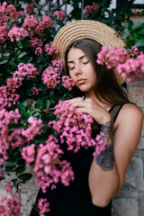 Brunette girl with long hair in hat surrounded with pink flowers 