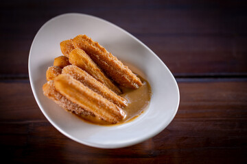 Churros sticks with caramel in a wooden background