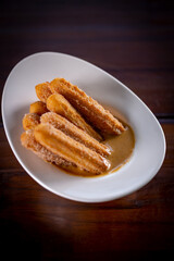 Churros sticks with caramel in a wooden background