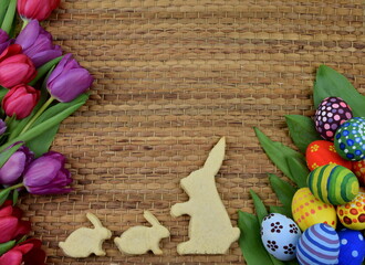 tulips, painted eggs and bunny shaped cookies on brown background 