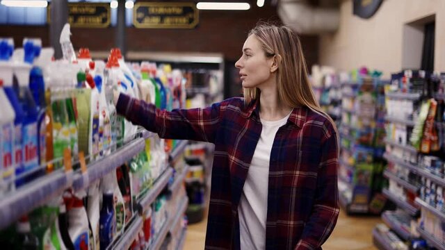 Woman choosing detergent at a household goods in the store, put it into cart