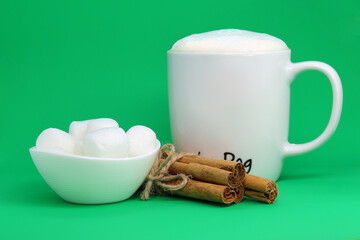 Coffee in a mug large marshmallow and cinnamon on a green background