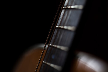 Close up of a steel strung guitars rosewood fretboard or fingerboard.Shot against a dark...