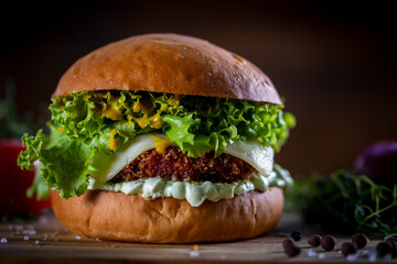 Craft crispy chicken burger with cheese, lettuce, tomato and sauce on wooden background