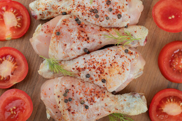 Close up photo raw chicken drumstick and fresh tomato on wooden board