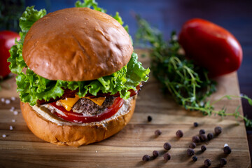 Craft beef burger with cheddar, bacon, lettuce and sauce on wooden background