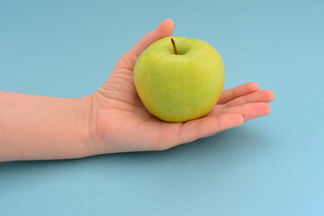 green apple on woman's hand on the blue background