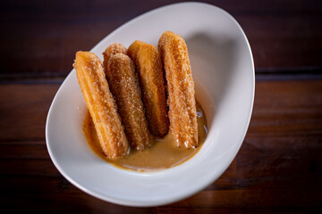 Churros sticks with caramel in a wooden background
