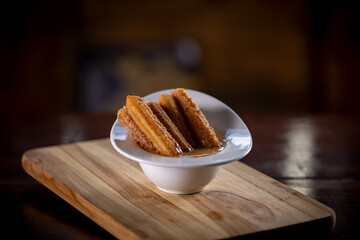 Churros sticks with caramel in a wooden background