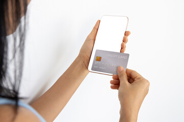 A woman shopping online on her sofa at home with a smartphone using a silver credit card. And use your credit card to tap the screen to verify the identity. Concept about business. over shoulder shot