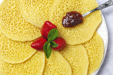 Homemade traditional moroccan baghrir with honey, strawberries and mint from above