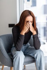Woman crying suffering from depression sitting on a chair. Bad mood and energy decline. Headaches