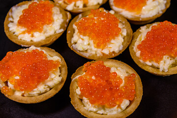 Tartlets with red caviar on a black plate. Festive food