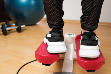 Back view on the woman feet in sneakers doing exercising on the twist stepper or stair stepper machine at home during lockdown. Keep fit. Cardio at home. 