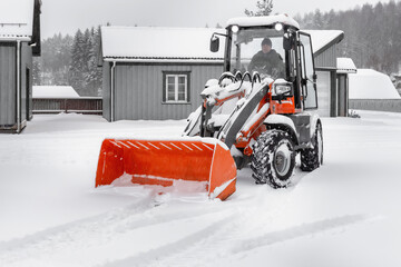 Little red tractor with snowplow removing snow during  snowfall. Blizzard weather conditions....
