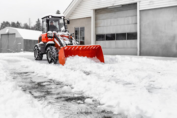 Little red tractor with snowplow removing snow during  snowfall. Blizzard weather conditions....
