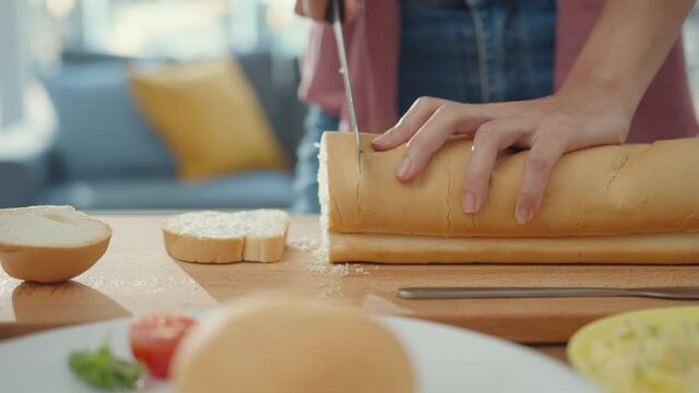 Hands of young Asian woman chef holding knife cutting whole grain bread on wooden board on kitchen table in house. Fresh homemade bread production, Healthy eating and traditional bakery concept.