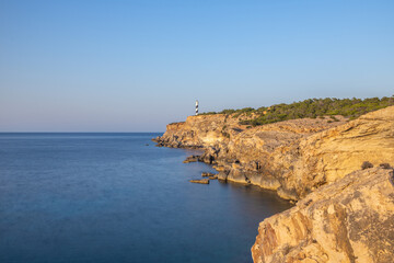 Fototapeta na wymiar Faro en el borde de un acantilado con un mar suavizado por una larga exposición y un cielo de verano azul eléctrico 