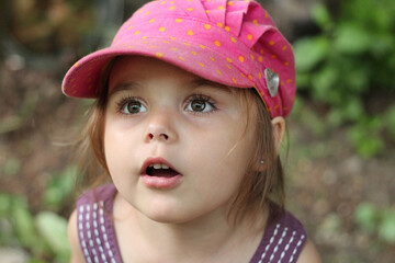 Happy little funny emotional girl in a cute pink cap looks with surprise opening her mouth