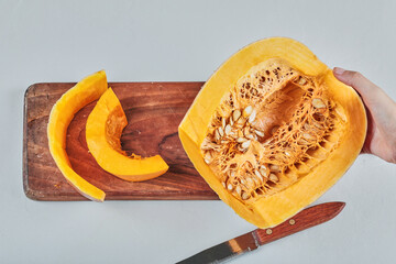 Hand holding pumpkin on wooden chopping board with knife