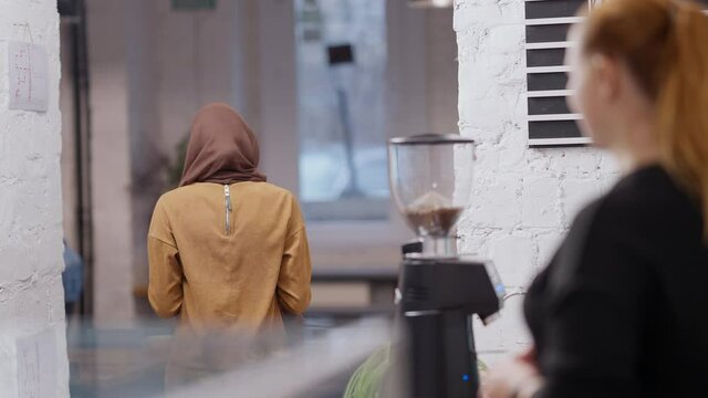 Portrait of happy Muslim young woman receiving takeaway coffee in cafeteria and leaving. Positive smiling Middle Eastern client in cafe. City lifestyle and service concept.