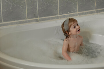 little smiling child sits in a large bubble bath. View from above. Flatley