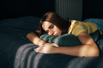 Tired young woman in casual clothes lying in bed
