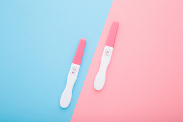 Pregnancy tests with one stripe and two stripes on light blue pink table background. Pastel color. Negative and positive result. Closeup. Two sides. Top down view.