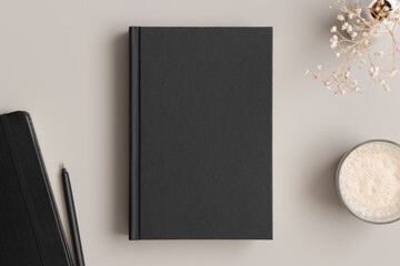 Black book mockup with a gypsophila, coffee and workspace accessories on the beige table.