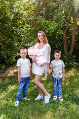 happy mother and three children. envelope with newborn baby in hands woman on natural green background