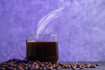 Glass espresso coffee cup, scattered roasted coffee beans, colored background