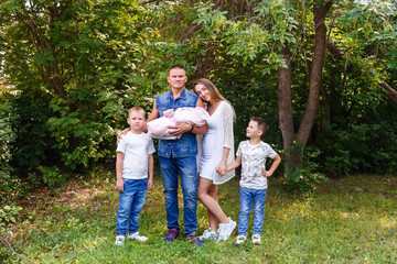 Obraz premium Happy parents and two children of preschoolers and newborn baby washed into the camera on a natural green background in the summer