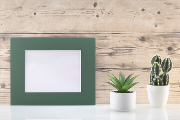 Modèle de cadre photo blanc avec espace vide pour logos, inscription publicitaire. Cadre en mode paysage sur un espace de travail avec des plantes vertes. Ambiance zen.