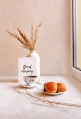 Good morning. A cup of tea on the window, dry reed in a vase, three golden cupcakes on a saucer. Concept of a feeling of coziness at home.Minimal, stylish, trend concept with neutral colors.